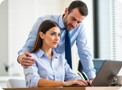 A female employee looking uncomfortable as a male colleague places his hand on her shoulder in a professional office setting, illustrating workplace harassment awareness.