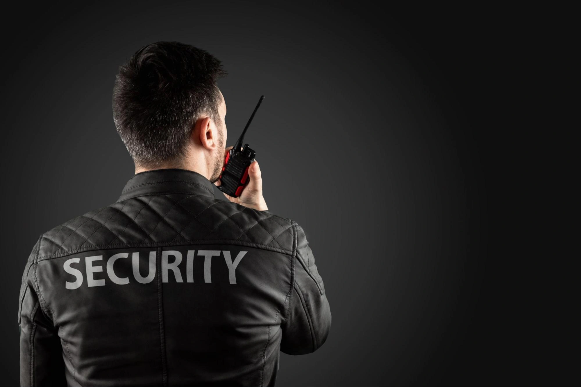 Security guard in a black jacket using a walkie-talkie for communication.