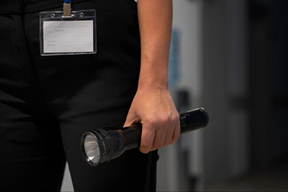 Close-up of a security guard’s hand holding a flashlight with ID badge visible, highlighting essential patrol tools taught in Guard Training’s courses.