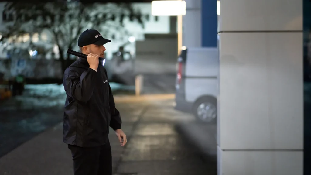 Security guard performing security guard duties while patrolling assigned areas at night with a flashlight outside a commercial building