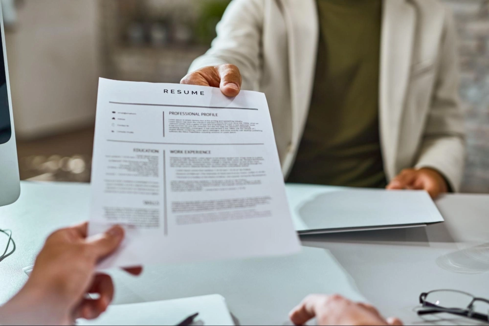 Close-up of a person handing over a resume during a security guard job interview, emphasizing hiring process in Guard Training programs