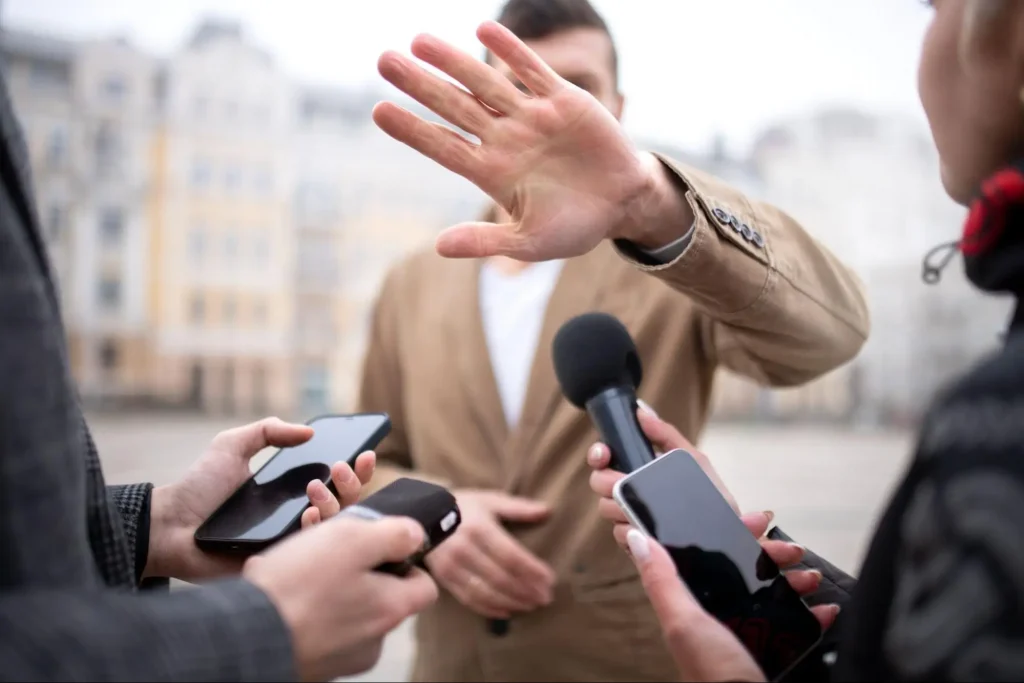 Person raising a hand to stop reporters, demonstrating conflict de-escalation techniques taught in security guard training
